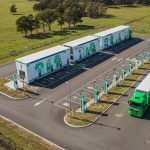 A modern electric truck parked at a high-tech charging station during twilight. The sleek, illuminated station features advanced charging equipment, emphasizing the shift toward sustainable and eco-friendly transportation solutions in the logistics industry.