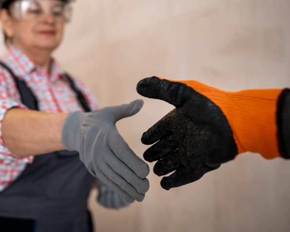 Two workers wearing safety gloves shaking hands, symbolizing teamwork and safety in the workplace.